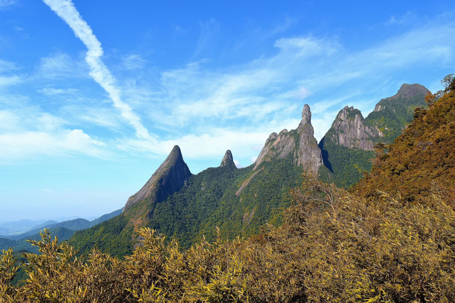 Pico Dedo de Deus com céu azul e vegetação de altitude em primeiro plano, Teresópolis