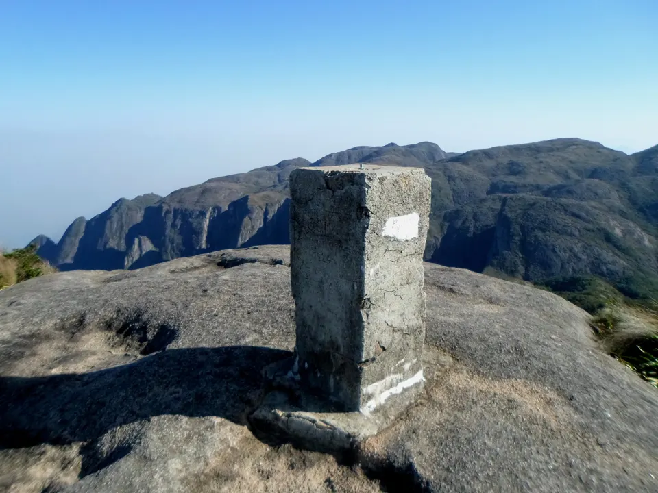 Marco geodésico no cume da Pedra do Sino com montanhas ao fundo