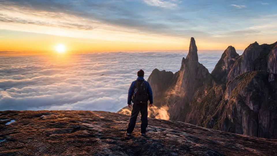 Montanhista no cume da Pedra do Sino ao nascer do sol acima do mar de nuvens