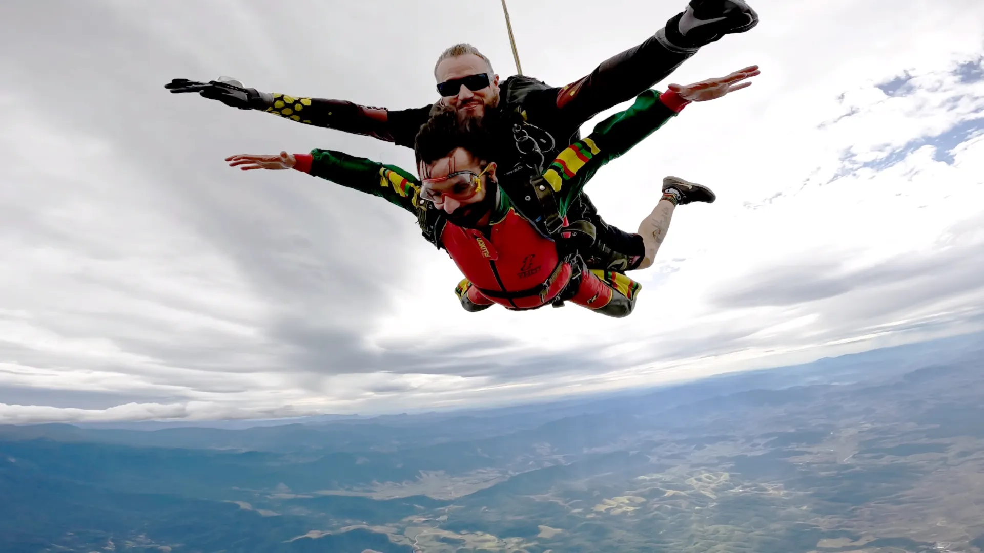 Salto duplo de paraquedas com instrutor sobre a Serra, céu nublado e montanhas ao fundo